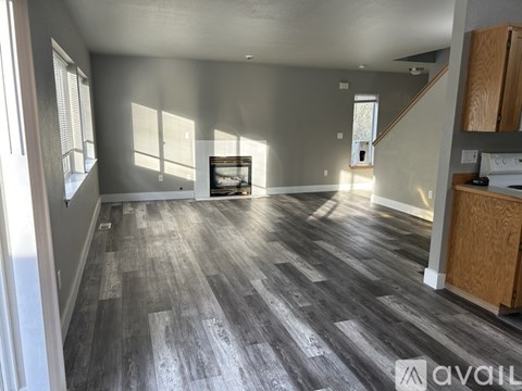 A spacious room with wooden flooring and a staircase in the background.