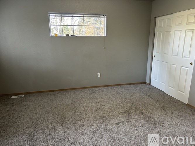 A room with a carpeted floor, a window with a view of trees, and a white door.