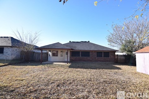 A house with a brown roof and a white door is surrounded by a fence and a grassy yard.