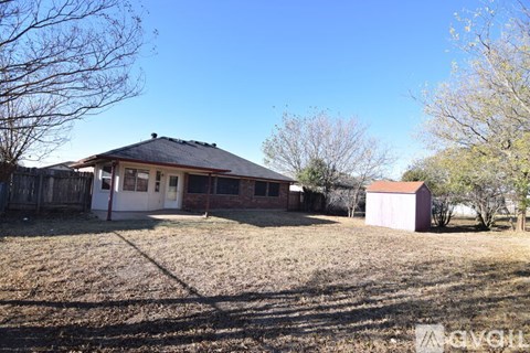 A house with a brown roof and a white door is surrounded by a fence and trees.