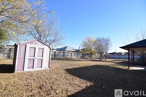A small purple shed sits in a field with a fence in the background.