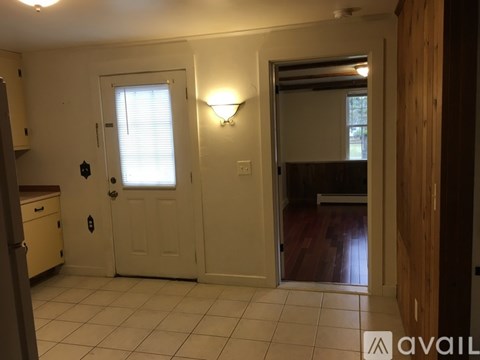 A room with a white door, a window with blinds, and a lamp on the wall.