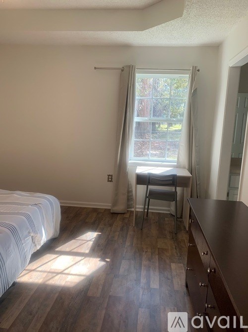 A room with a bed, a desk, and a window with sunlight coming through.