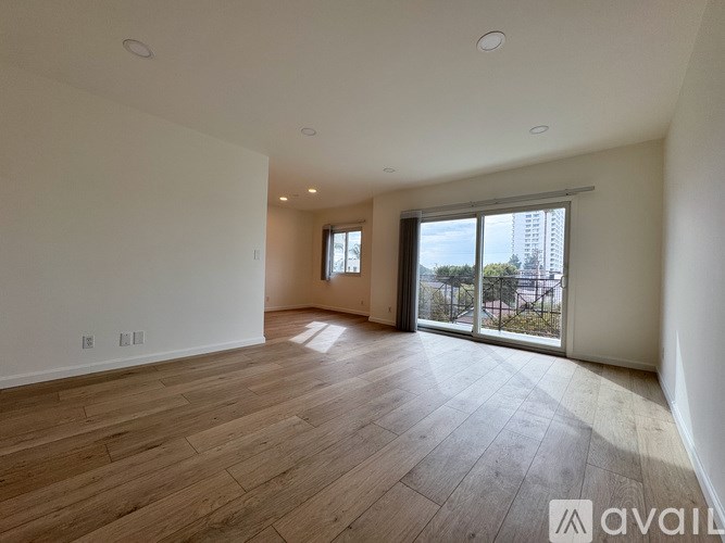A spacious room with wooden flooring and a large window overlooking a cityscape.