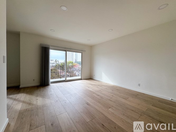 A spacious room with wooden flooring and a large window with a view of the city.
