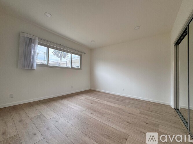 A spacious room with wooden flooring and a window with curtains.