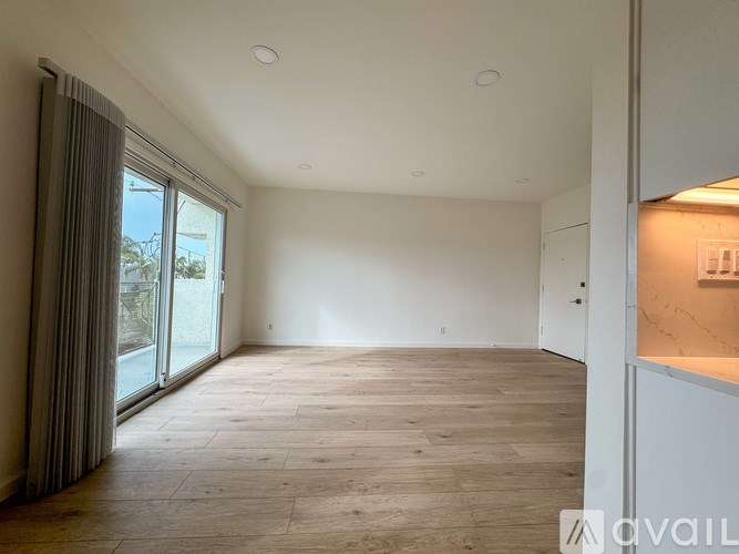 A spacious room with wooden flooring and a sliding glass door leading to a balcony.