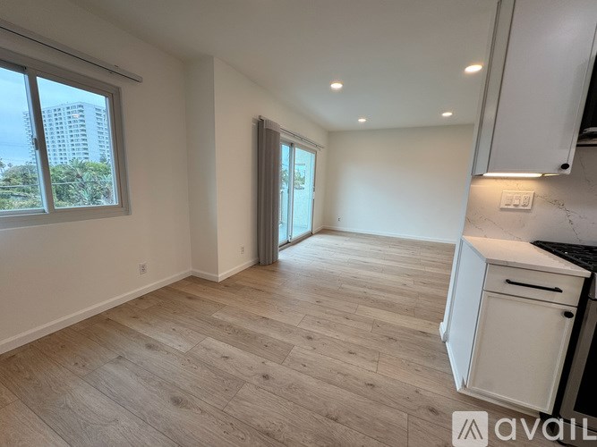 A spacious room with wooden flooring and a large window overlooking a cityscape.