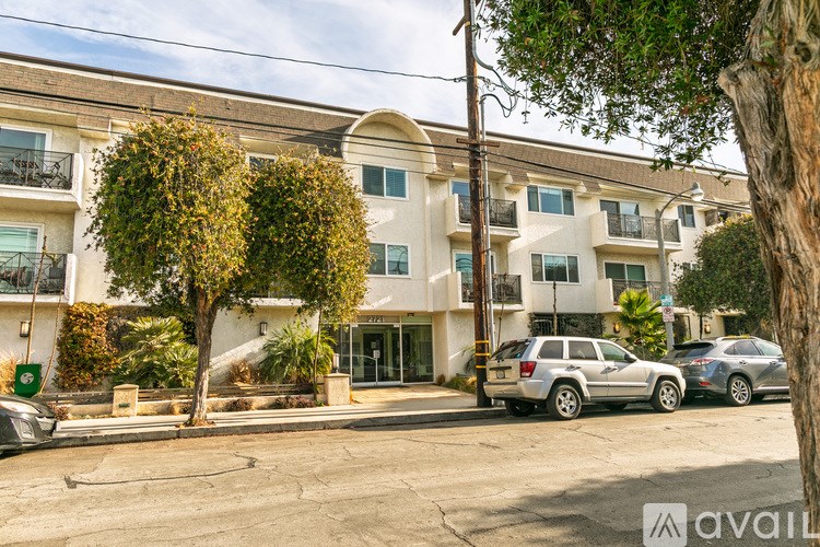A silver car is parked in front of a two-story building with a balcony.