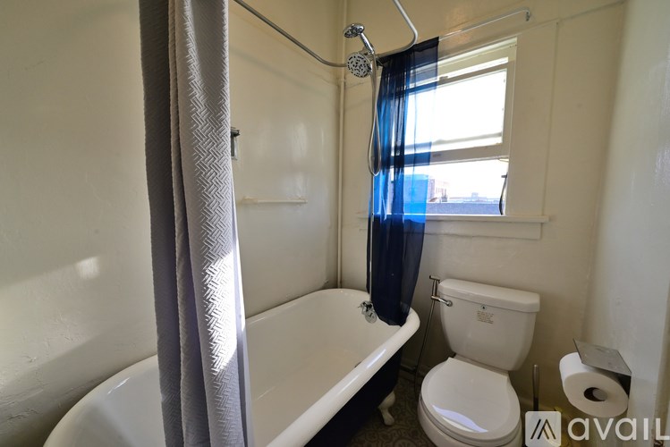 A bathroom with a toilet, bathtub, and a window with blue curtains.