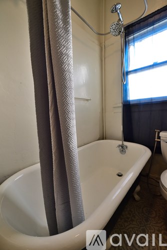 A white bathtub with a shower head and a grey curtain.