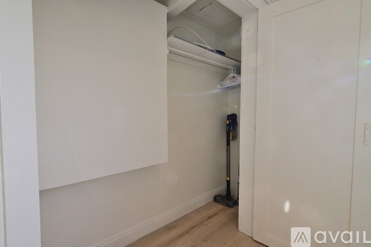 A vacuum cleaner is leaning against the wall in a room with white walls and wooden flooring.