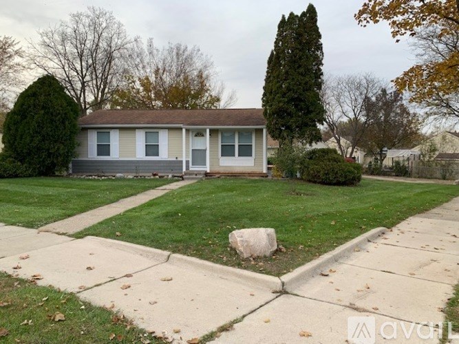 A house with a grey roof and a white door is surrounded by a green lawn.