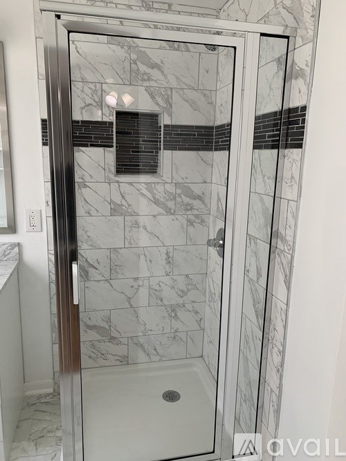 A bathroom with a marble tile shower and a glass door.