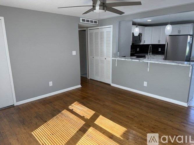 A room with a ceiling fan and a kitchen area in the background.