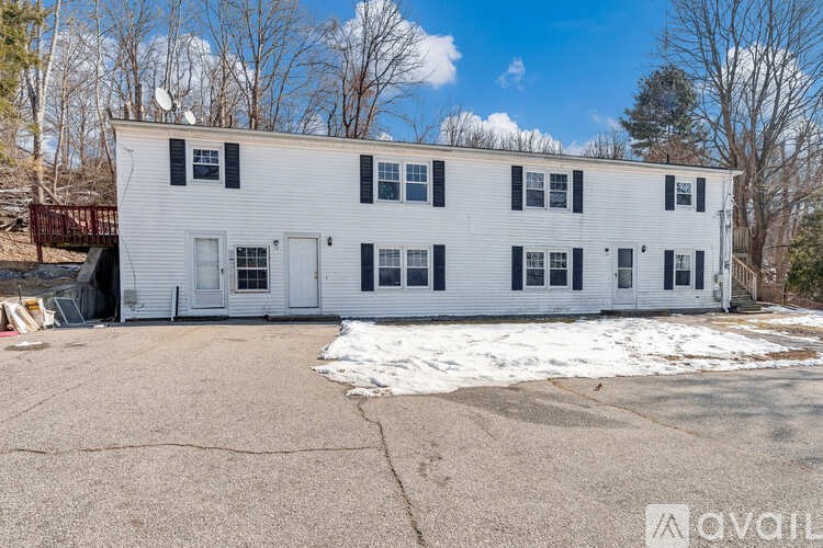 A white two-story house with a black roof and a driveway in front.