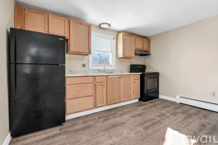 A black fridge sits in a kitchen with wooden cabinets and a window.