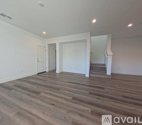 A spacious room with wooden flooring and a staircase in the background.