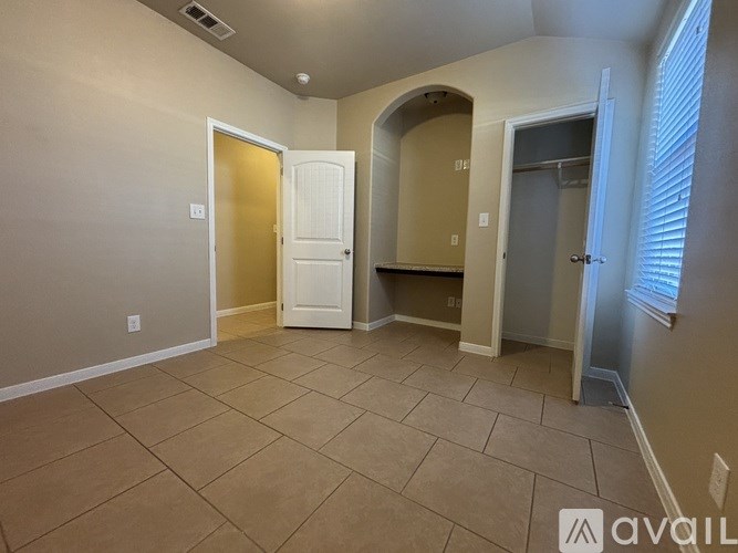 A room with beige walls and a tiled floor with a white door and a window with blinds.