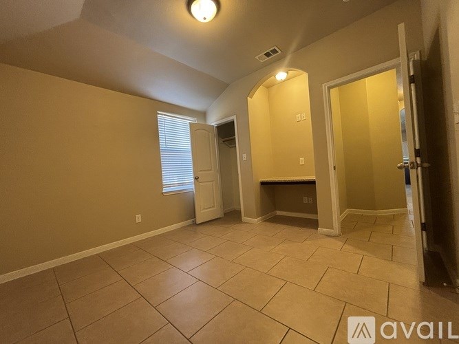 A room with beige walls and tiled flooring, with a doorway leading to another room.
