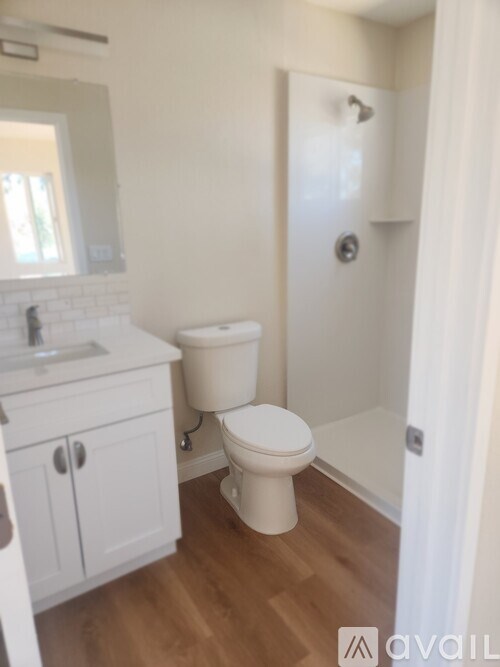 A white toilet sits in a bathroom with wooden floors and white walls.