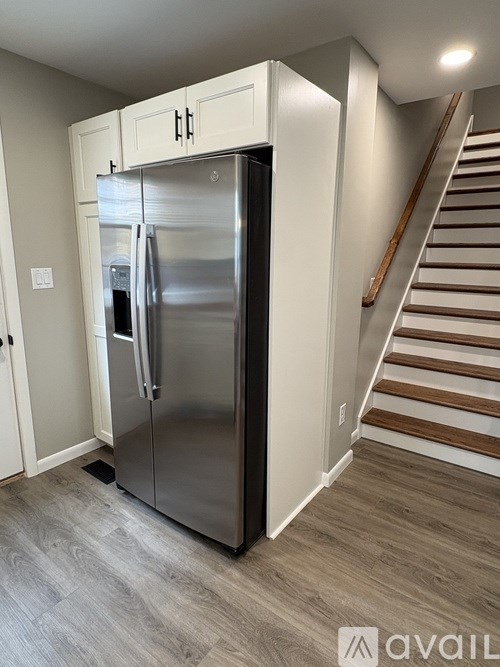A stainless steel refrigerator in a kitchen with a staircase in the background.