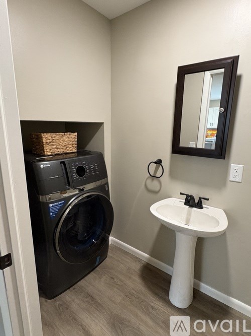 A bathroom with a white pedestal sink and a black washing machine.