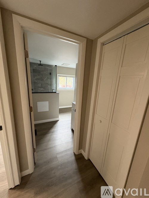 A hallway with a door on the left and a bathroom visible through the door.