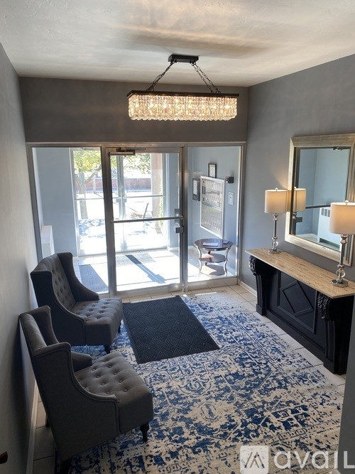 A room with a blue and white patterned carpet, two grey chairs, a wooden cabinet, and a chandelier.