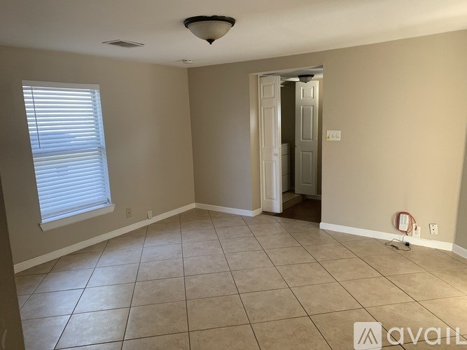 A room with beige walls and a tiled floor with a doorway leading to another room.