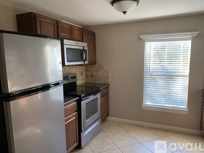 A kitchen with a refrigerator, microwave, oven, and a window with blinds.
