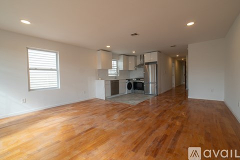A spacious room with wooden flooring and a kitchen area in the background.