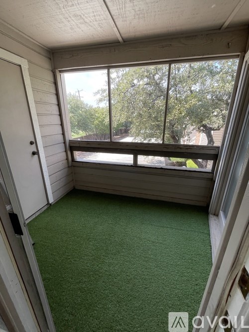 A room with a green carpet and a window overlooking a tree.