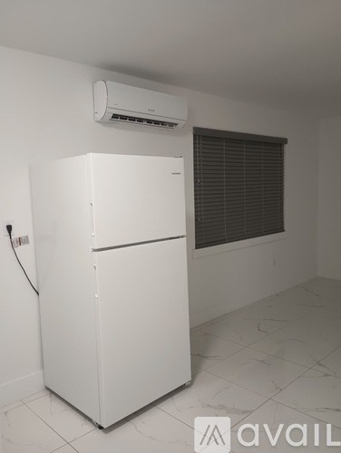 A white refrigerator in a room with a window and an air conditioner.