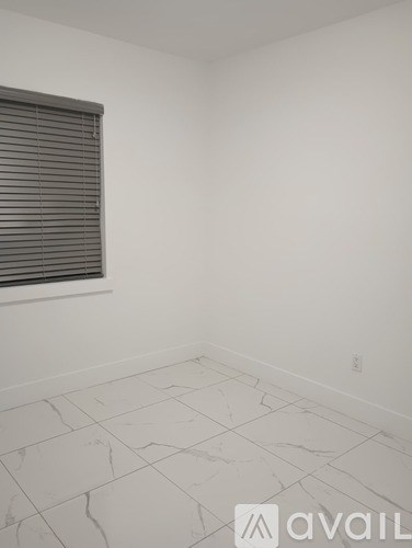 A room with a window covered by blinds and tiled flooring.