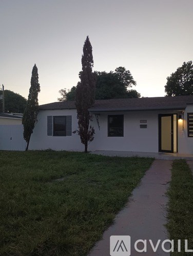 A white house with a brown door and a small garden in front.