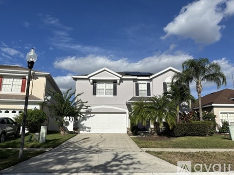 A house with a white garage door is in front of a palm tree.