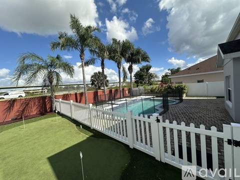 A white picket fence surrounds a pool area with a palm tree.