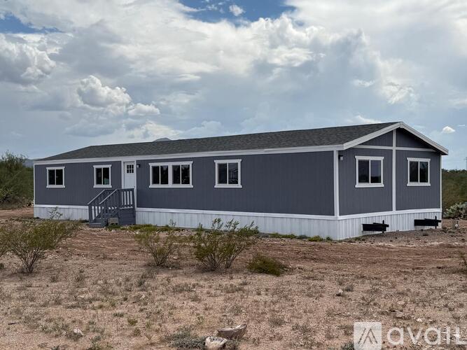 A grey house with a white base is situated in a dry, grassy area.