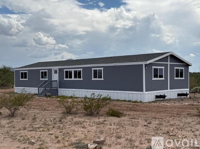 A grey house with a white base is situated in a dry, grassy area.