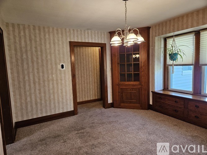 A room with a carpeted floor, a wooden door, and a chandelier hanging from the ceiling.