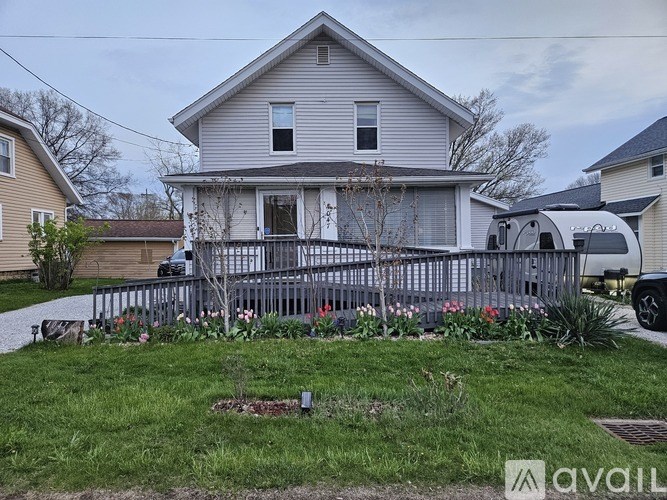 A house with a grey roof and a white door is surrounded by a fence and some plants.