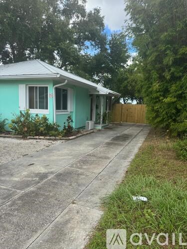 A blue house with a white door and windows is surrounded by greenery.