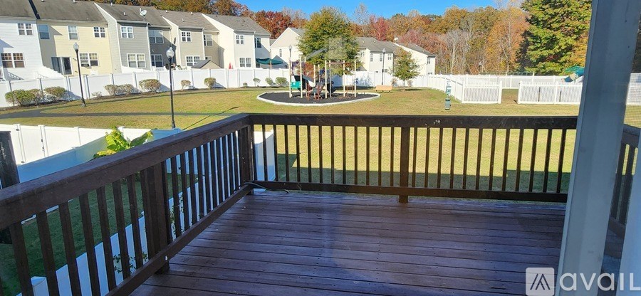 A wooden deck with a railing overlooks a grassy area and apartment buildings.