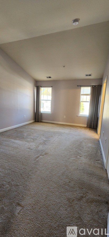 A spacious room with carpeted floor and two windows.