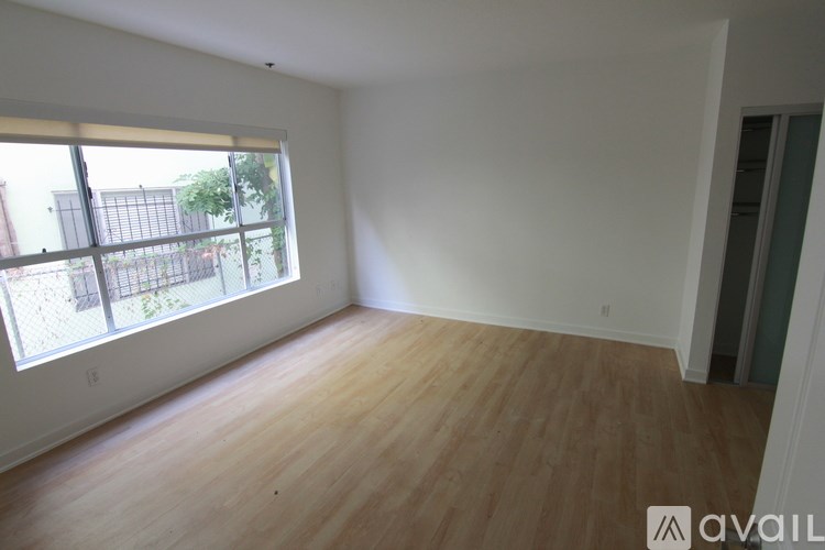 A room with wooden flooring and a large window overlooking a fenced area.