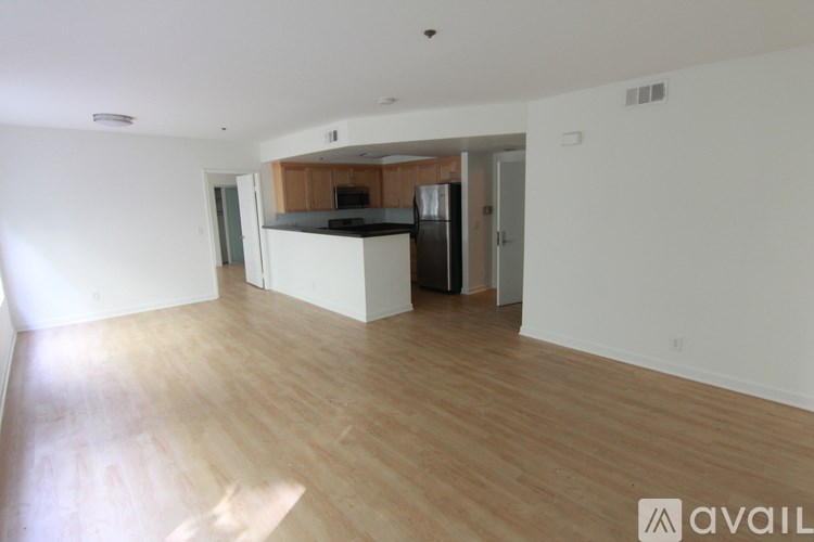 A spacious room with wooden flooring and a kitchen area in the background.
