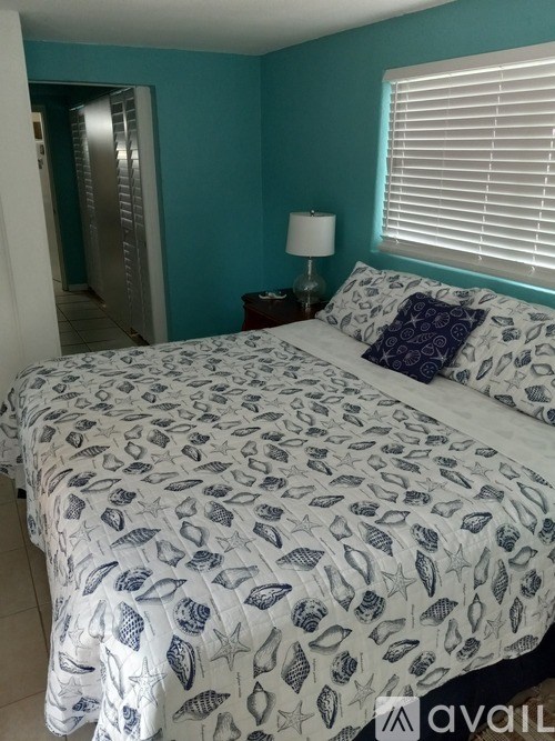 A bed with a white comforter and a blue pillow is in a room with a window.