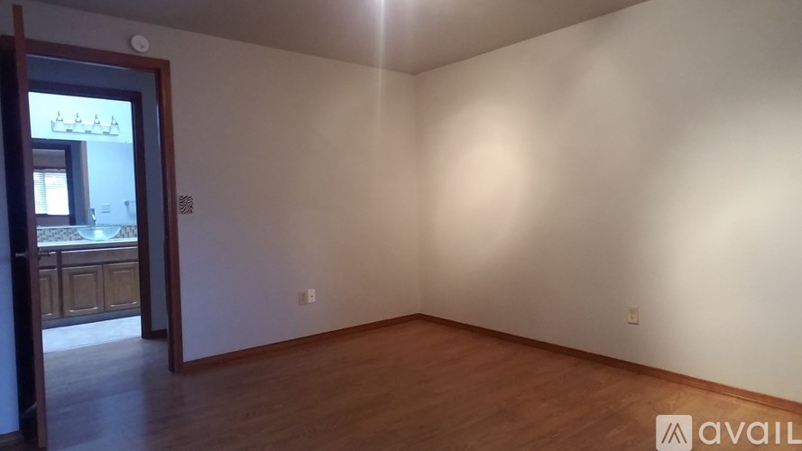 A room with wooden floors and white walls with a doorway leading to another room.
