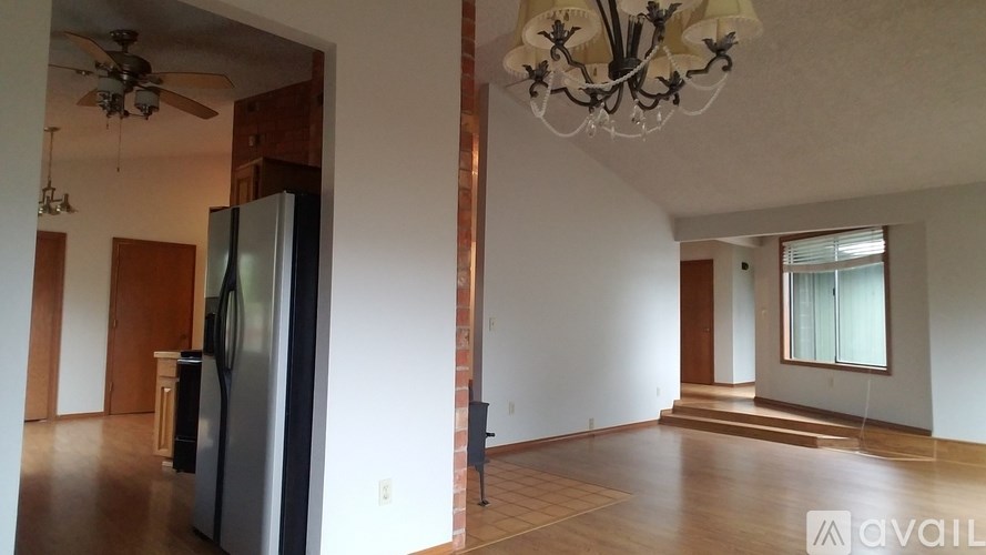 A spacious living room with a chandelier and a kitchen area with a refrigerator.